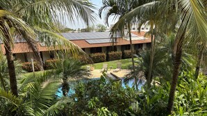 Una piscina rodeada de abundante vegetación, un edificio con techo de tejas y paneles solares.