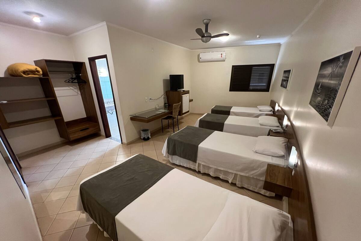 A hotel room with two beds, a desk, a chair, a ceiling fan, and a window with blinds.