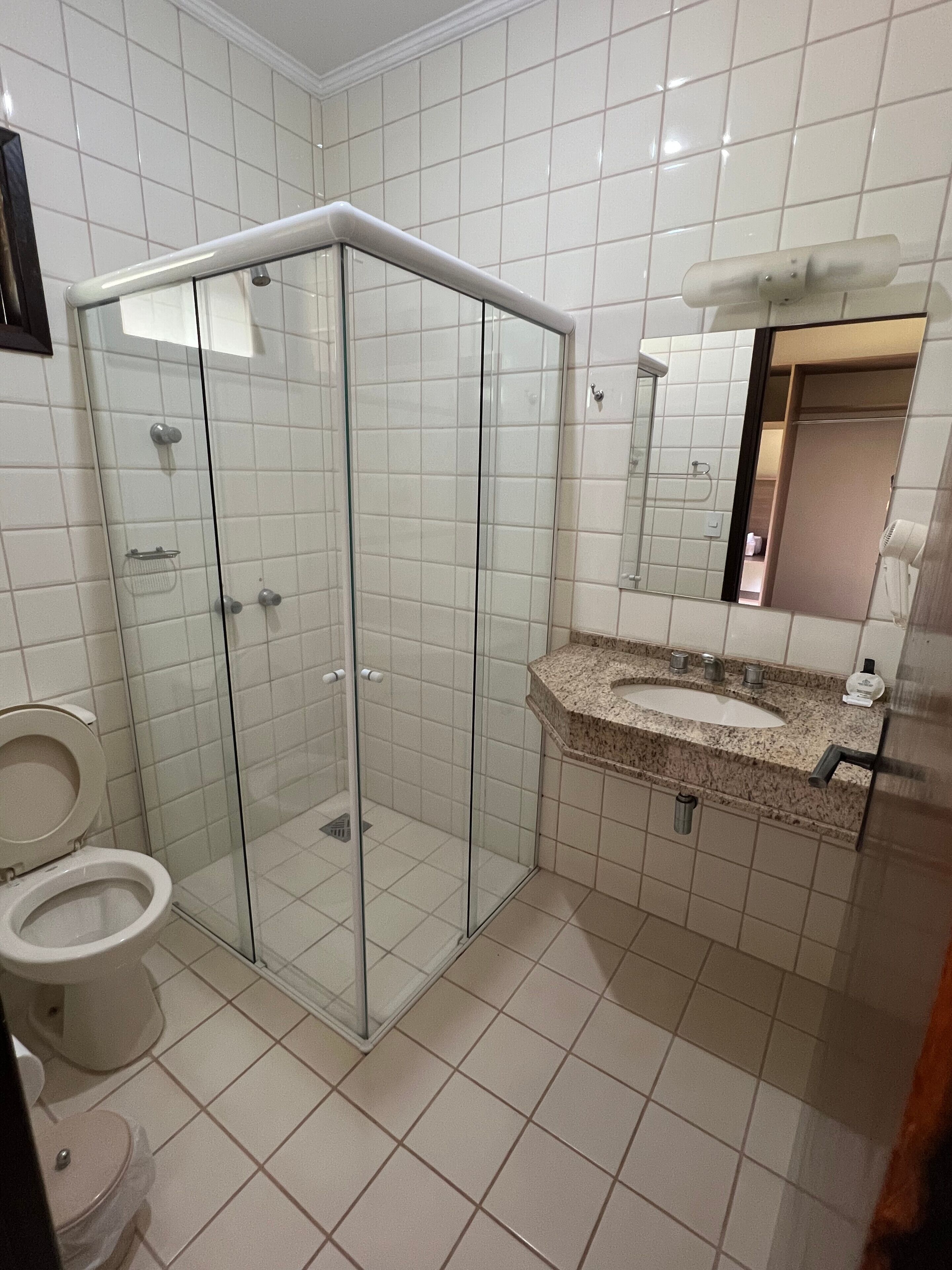 Casa de banho com cabine de duche envidraçada, lavatório com bancada de granito e espelho acima do lavatório.