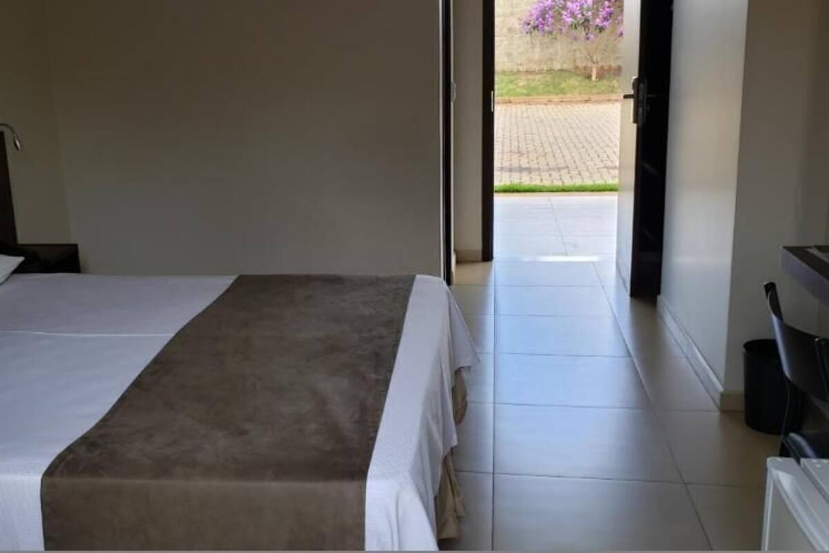 A hotel room with a bed, a nightstand, a desk, and a view of the outside.
