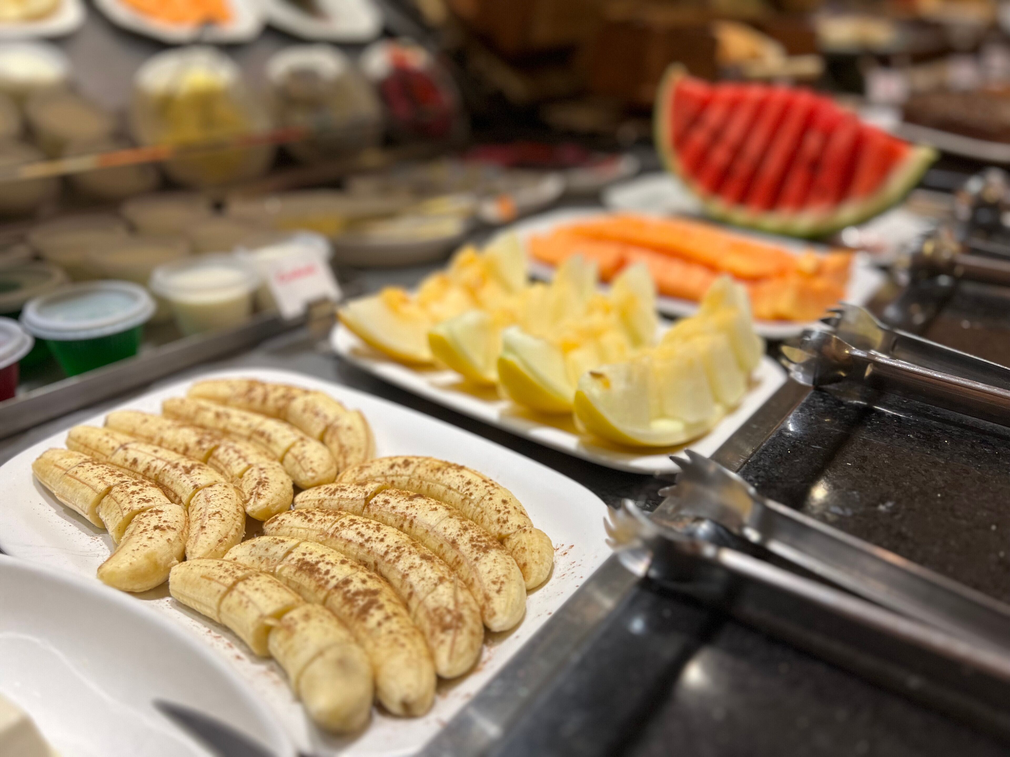 A buffet with various food items including bananas, watermelon, and other fruits.