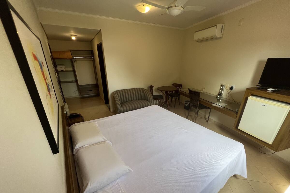 A hotel room with a bed, a desk, a chair, a television, and an air conditioning unit.