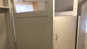 Een kamer met een stapelbed, een klein raam met gordijn en een deur naar een andere kamer.