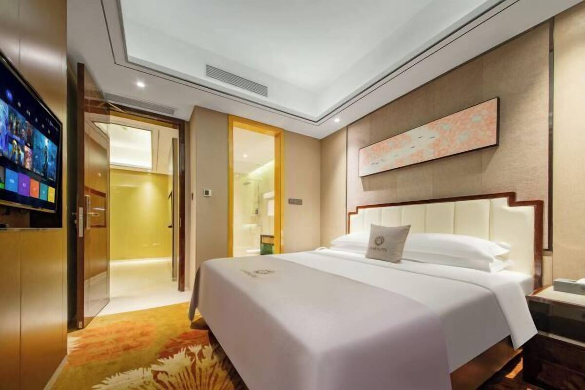 A hotel room with a bed, a television, a painting on the wall, and a door leading to another room.