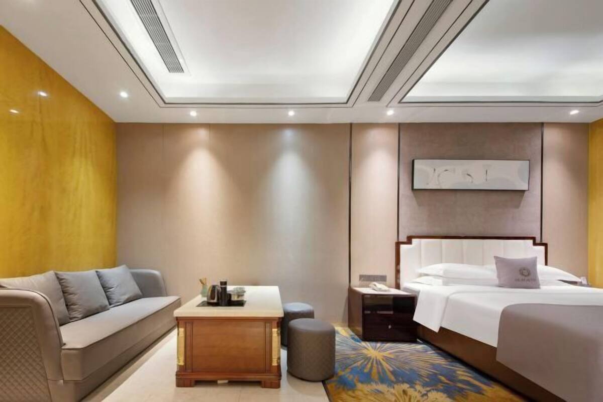 A modern hotel room with a sofa, a bedside table, a nightstand, a bed, and a ceiling with recessed lighting.