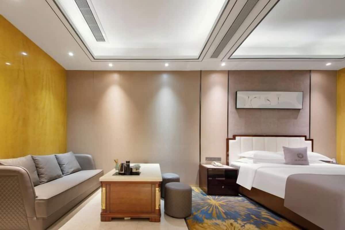 A modern hotel room with a sofa, a bedside table, a nightstand, a bed, and a ceiling with recessed lighting.