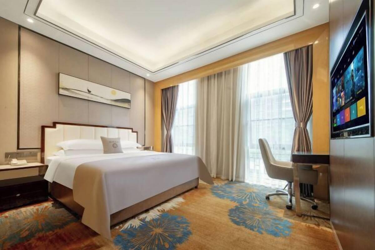 A hotel room with a large bed, a desk, and a TV.