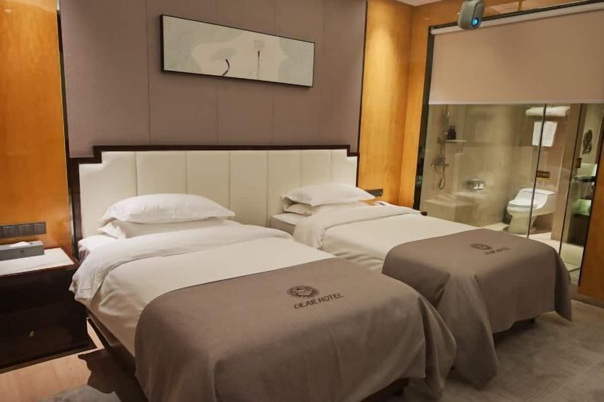 A hotel room with two beds, a large artwork on the wall, and a glass shower enclosure.