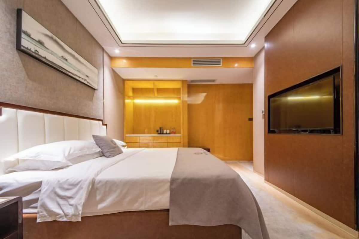 A modern hotel room with a bed, a flat-screen TV, a wooden cabinet, and a ceiling light.