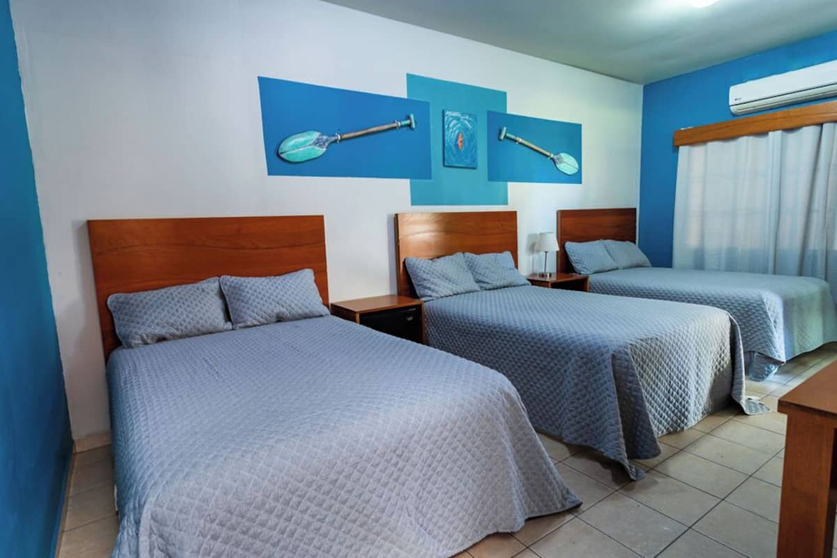 A hotel room with two beds, a wooden headboard, a nightstand, and a wall with three paddleboard paintings.