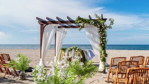 Decoración para boda en la playa, con un arco de madera, cortinas blancas y detalles florales.