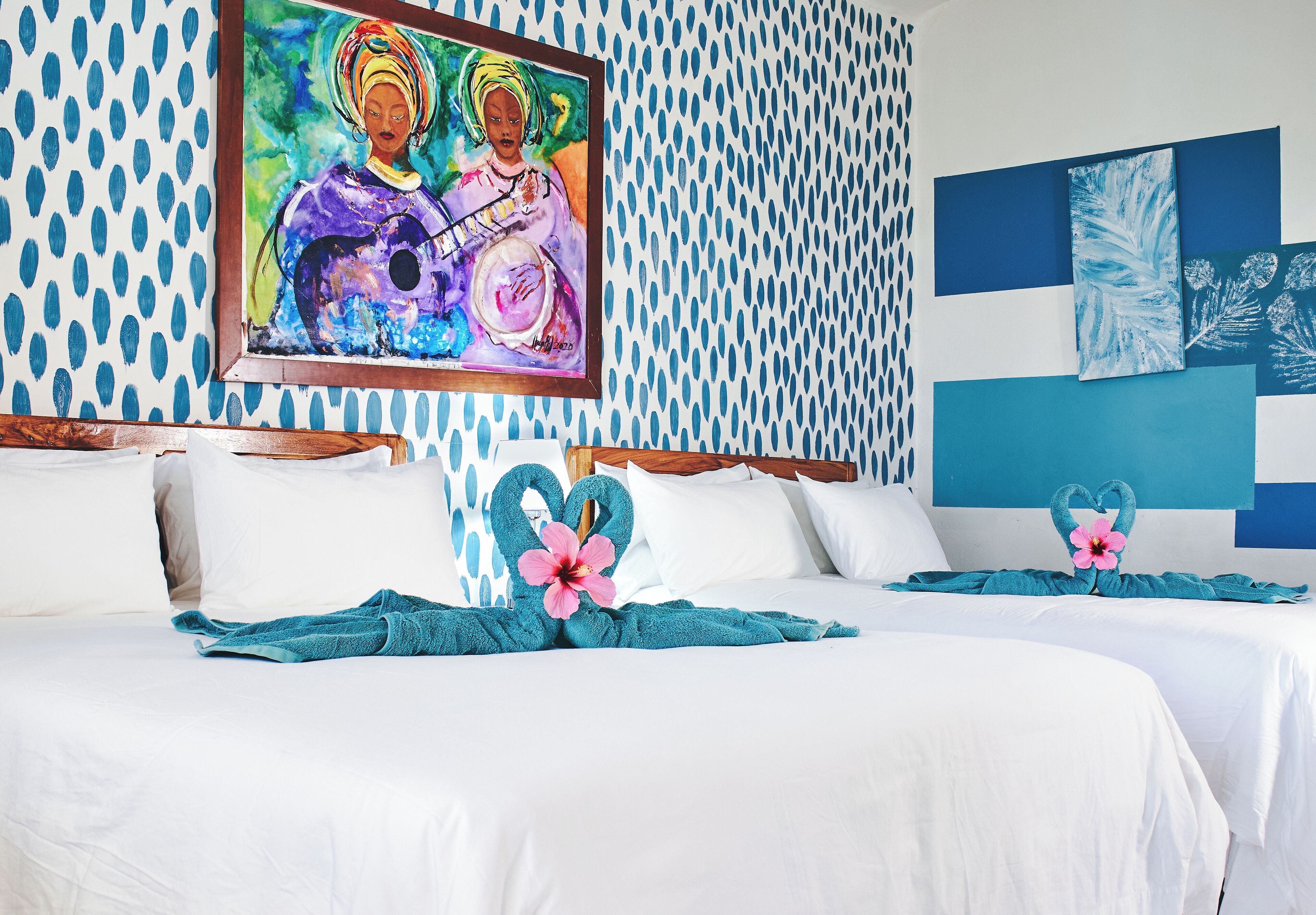 A hotel room with a patterned wall, a painting, and heart-shaped floral arrangements on the bed.