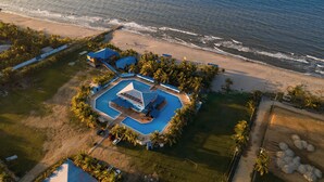 Vista aérea de un resort con una piscina grande, acceso a la playa y palmeras.