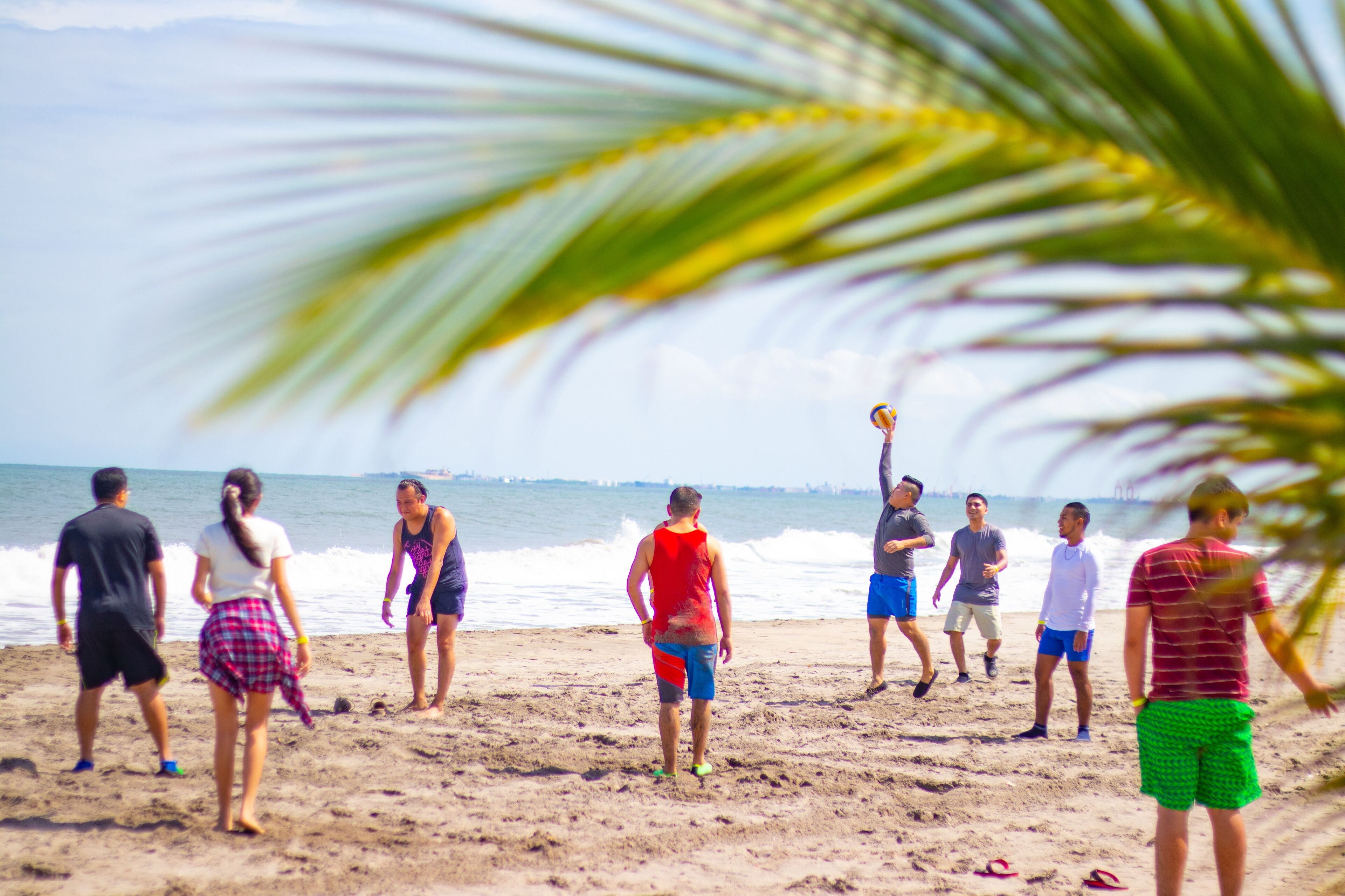 A group of people playing volleyball on a sandy beach with the ocean in the background.