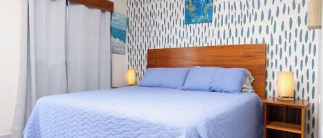 Ein Bett mit hölzernem Kopfteil, einer Wand mit Muster und einem Nachttisch mit Lampe.