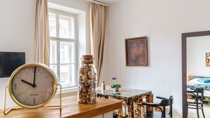 Een kamer met een houten eettafel, een klok, een vaas met bloemen en een schilderij aan de muur.