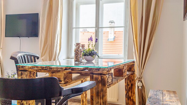 Een eethoek met een houten tafel en stoelen, een vaas met bloemen en uitzicht op een gebouw door een raam.