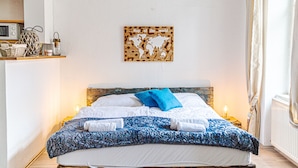 Een slaapkamer met een houten hoofdbord, een bed met wit en blauw beddengoed, een wereldkaart aan de muur en een nachtkastje met een lamp.