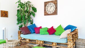 Een rustieke houten bank met kleurrijke kussens, een houten klok en een potplant.