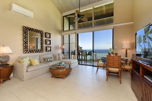 Relax in this spacious living room with ocean views, featuring a comfortable sofa, dining area, and large TV.