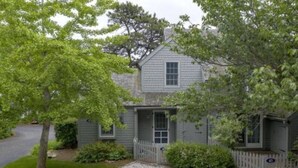 A two-story house with a front porch, a gravel driveway, and a picket fence. - Cape Cod Cottage steps from Private Beach (Mashpee)