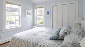 A bedroom with a large bed, two windows, a white door, and a small table. - Cape Cod Cottage steps from Private Beach (Mashpee)