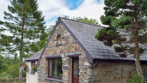 A stone cottage with a sloped roof, a front door, and a window with a flower box. - Old Chapel Cottage - Dinas Country Club (Dinas Cross, near Newport)