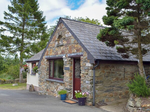 A stone cottage with a sloped roof, a front door, and a window with a flower box.