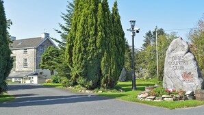 A stone building with a stone facade, a large coniferous tree, and a sign for Dinas Country Club. - Old Chapel Cottage - Dinas Country Club (Dinas Cross, near Newport)