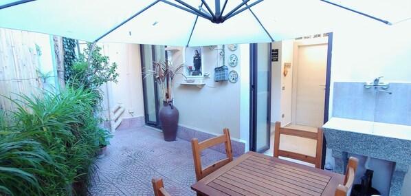 A patio area with a table and chairs, a large vase, and a wall with a mirror and decorative plates.