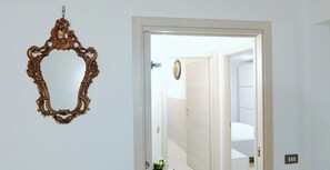 A doorway leading to a room with a bed and a wall-mounted mirror.