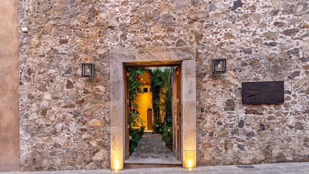 Un bâtiment en pierre avec une porte d’entrée donnant sur un intérieur éclairé d’une lumière jaune.