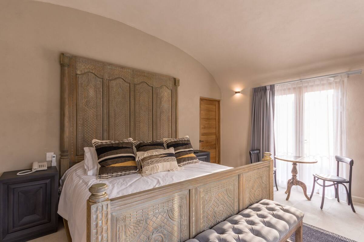 Une chambre à coucher avec un grand lit, une table de chevet, un banc, une petite table et une chaise.