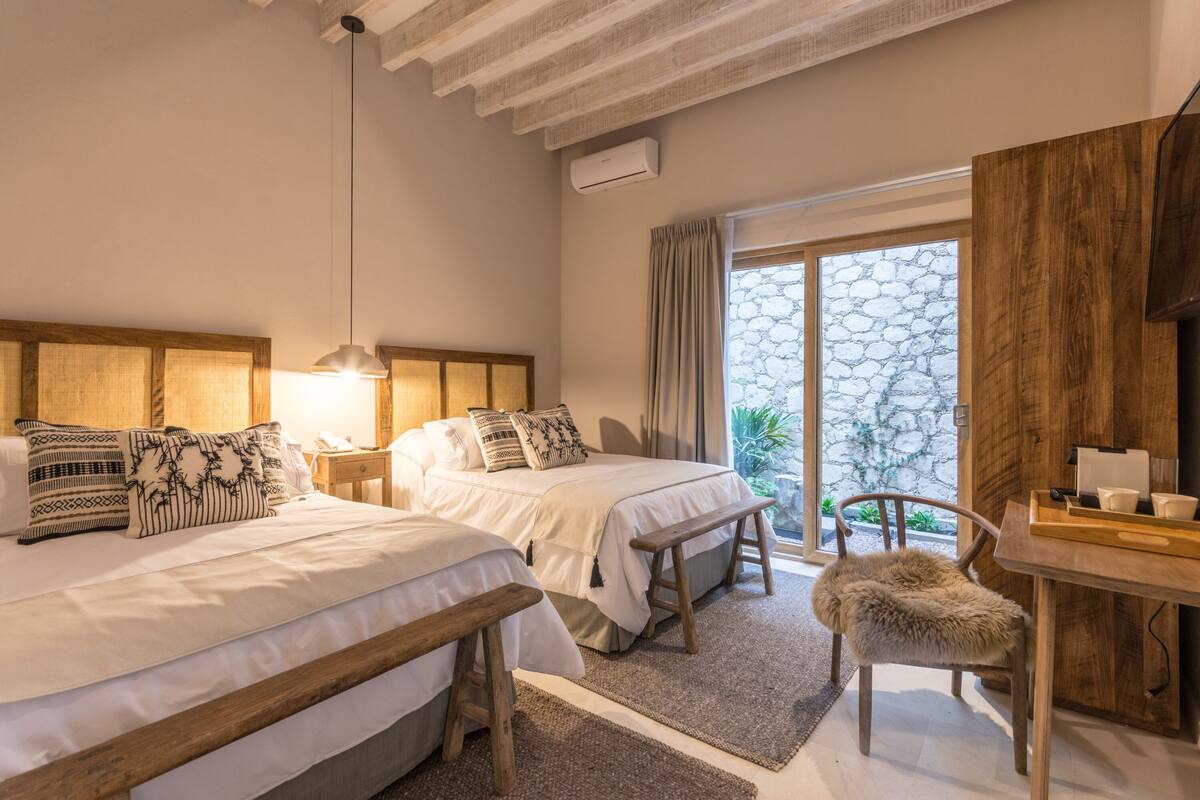 Une chambre d’hôtel avec deux lits, un banc en bois, une petite table et une chaise.