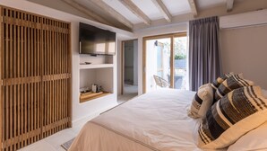 Une chambre dotée d’un grand lit, d’un téléviseur fixé au mur, d’une cloison en lattes de bois et d’une porte-fenêtre coulissante donnant sur un espace extérieur.