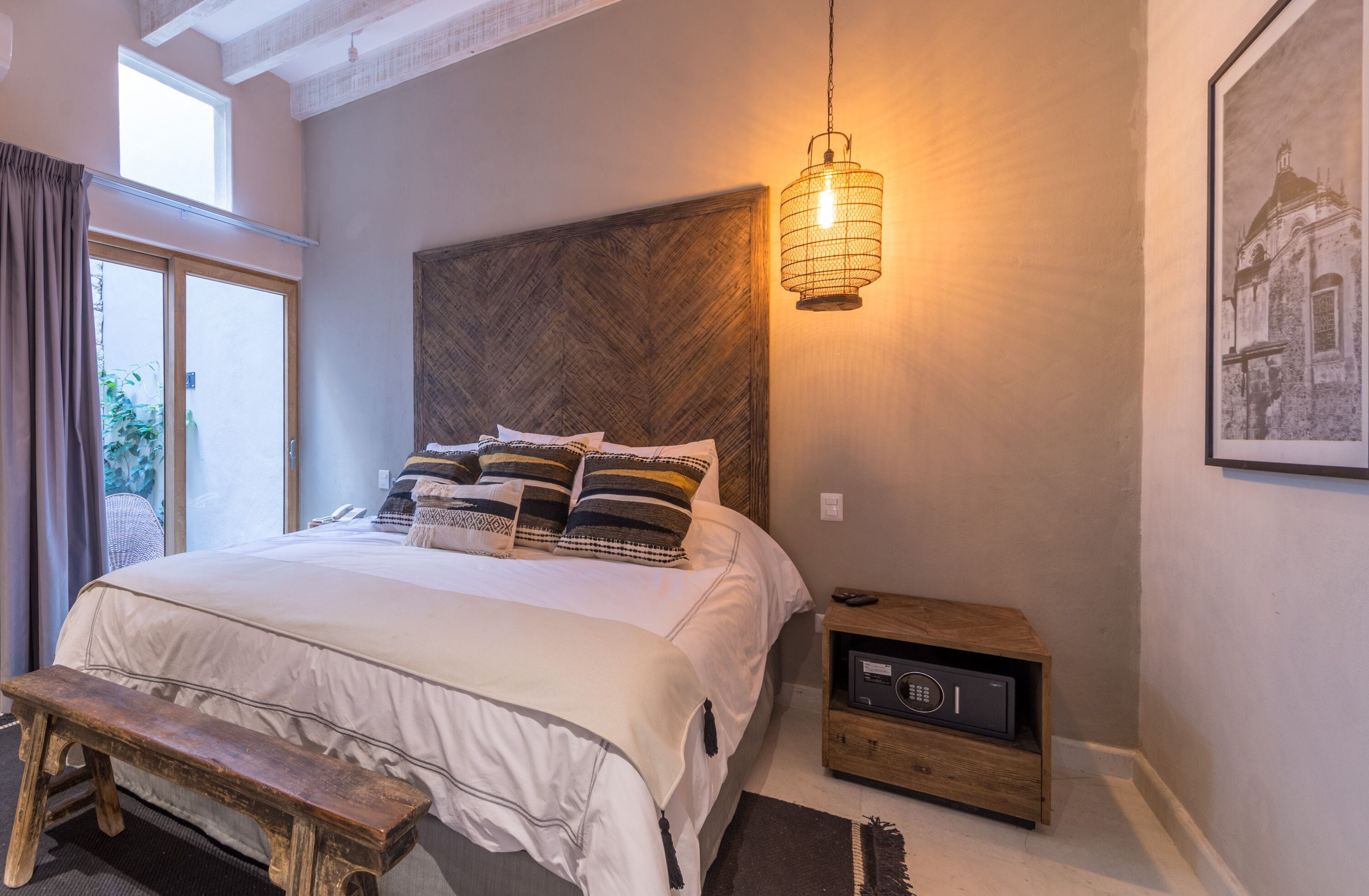 Un dormitorio con una cama grande, un cabecero de madera, una mesita de noche con una radio y una lámpara colgante.