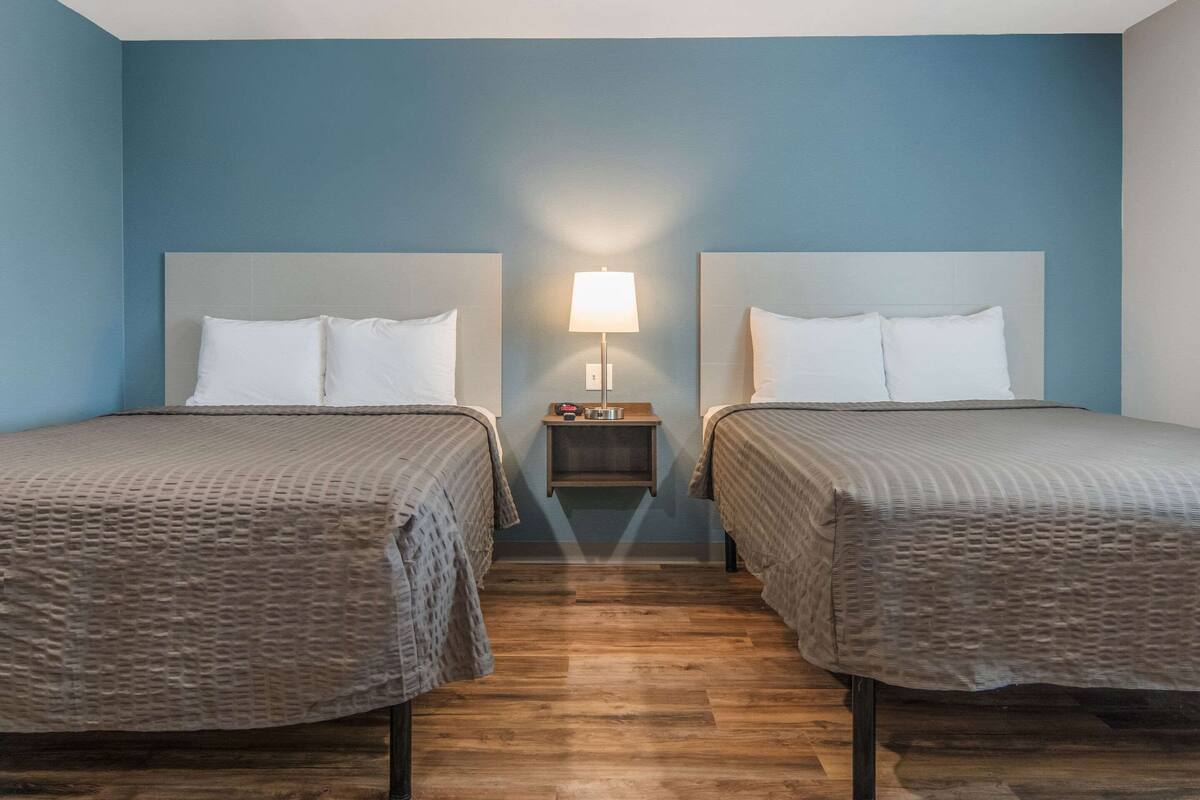 Une chambre d’hôtel avec deux lits, une table de chevet et une lampe fixée au mur.