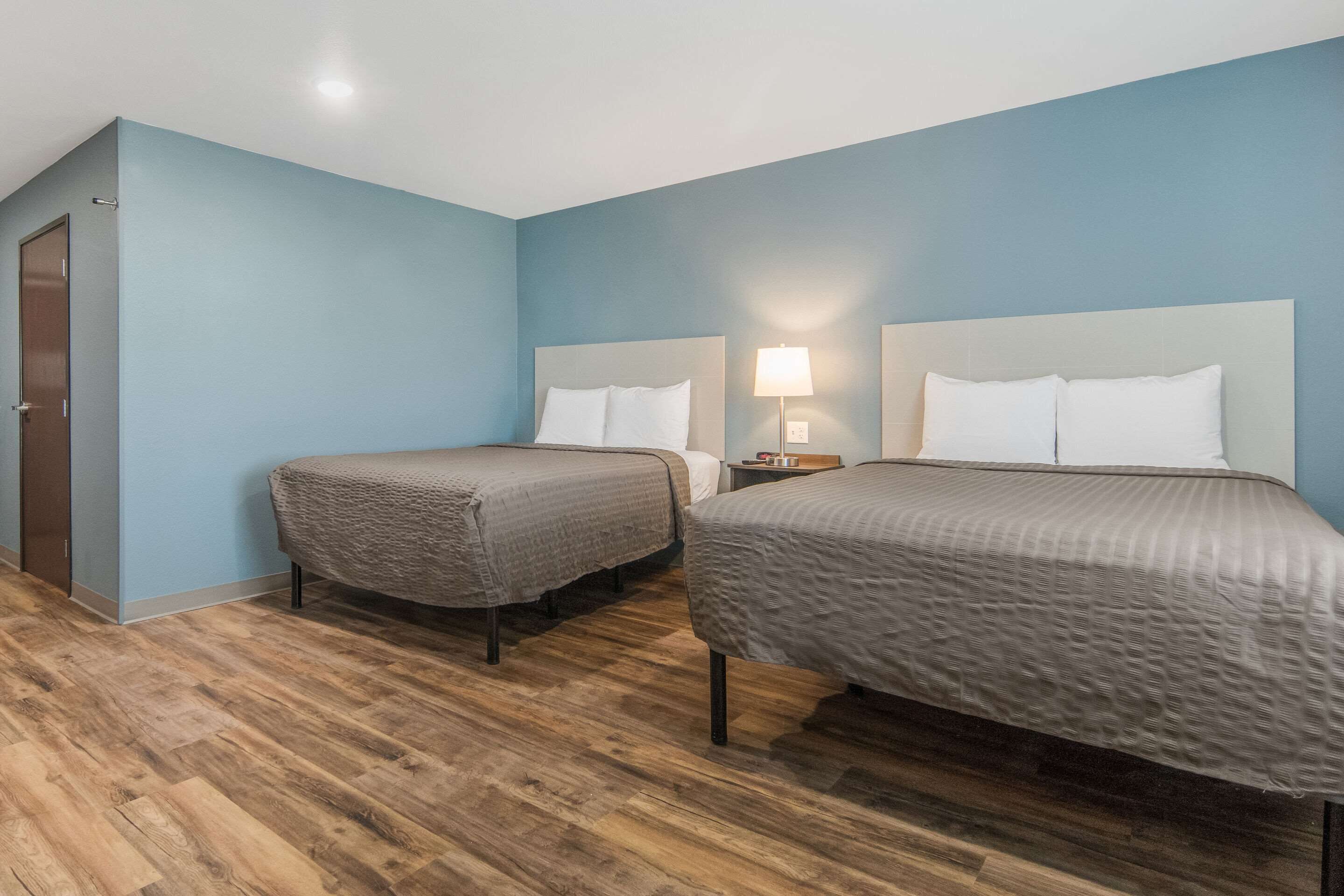 A hotel room with two beds, wooden flooring, and a blue wall.