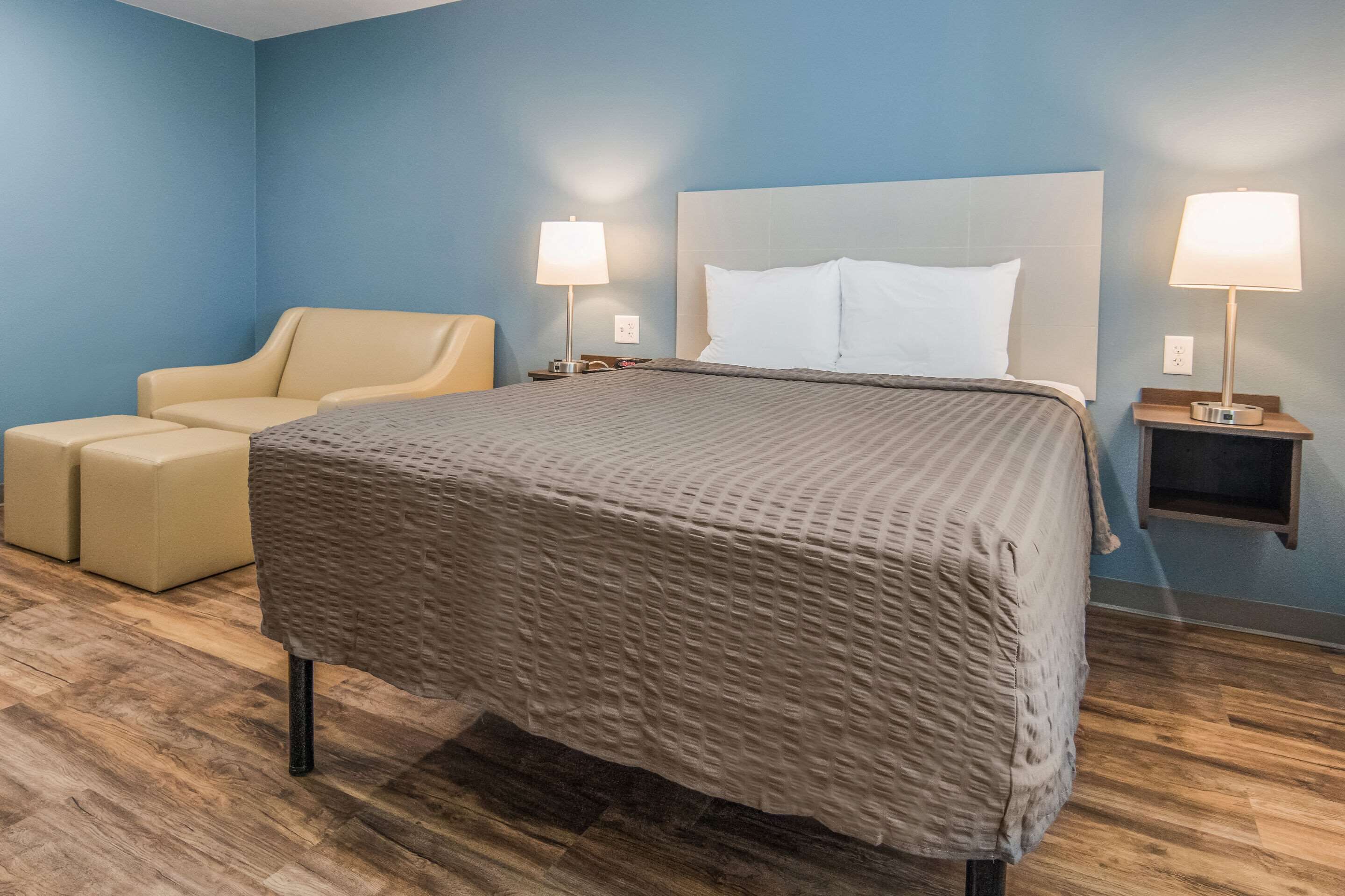 Una camera d'albergo con un letto grande, una poltrona, due comodini con lampade e una parete blu.