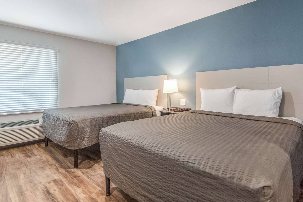 Une chambre d’hôtel avec deux lits, une fenêtre avec des stores, un radiateur et une table de chevet avec une lampe.