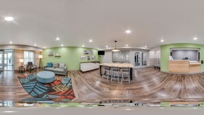 A spacious, modern interior with a curved wooden floor, a central dining area, and a reception desk. - WoodSpring Suites North Ft Worth Alliance TX Speedway (Fort Worth)