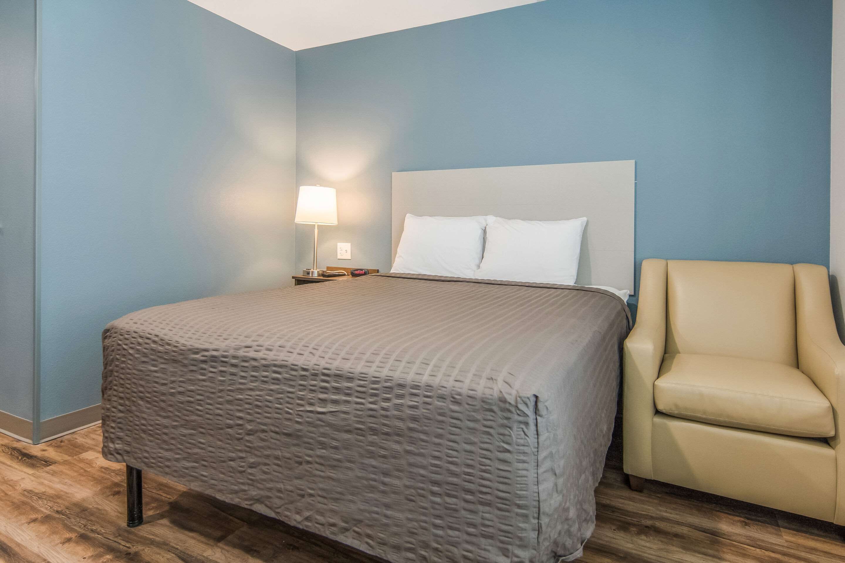 A bedroom with a bed, a nightstand, a lamp, and a chair.