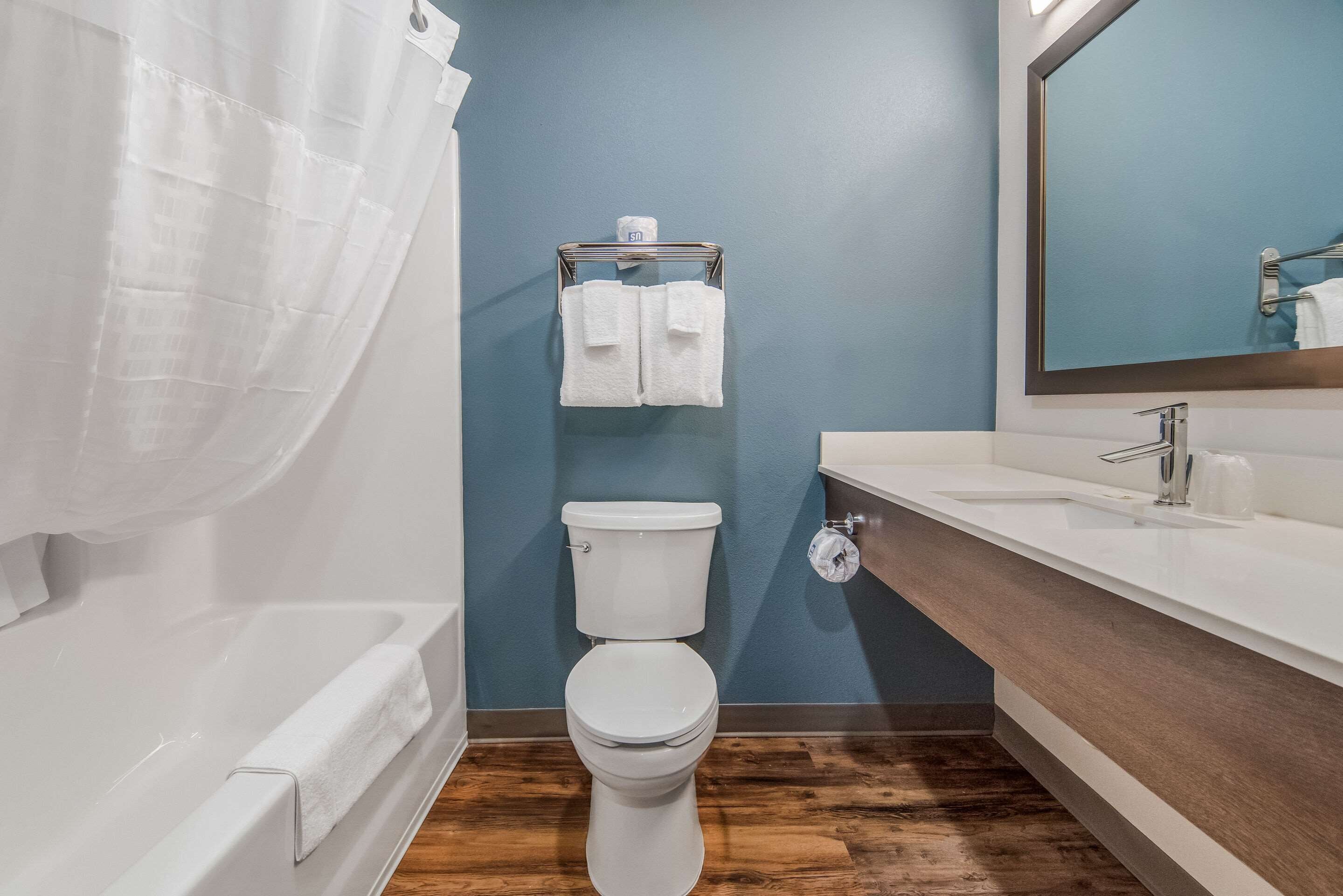 A bathroom with a white toilet, a wooden floor, a white bathtub, and a sink with a mirror.