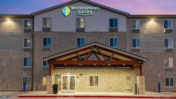 A multi-story hotel with a stone facade, a covered entrance, and a sign reading "Woodspring Suites." - WoodSpring Suites North Ft Worth Alliance TX Speedway (Fort Worth)