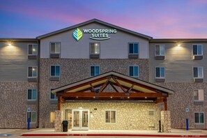 Un hotel de varios pisos con fachada de piedra, una entrada cubierta y un letrero que dice "Woodspring Suites".