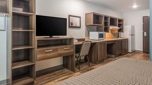 A compact hotel room with a bed, a desk with a computer, a TV, a microwave, and a refrigerator. - WoodSpring Suites North Ft Worth Alliance TX Speedway (Fort Worth)