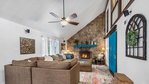 A spacious living room with a stone fireplace, a blue door, and a ceiling fan.