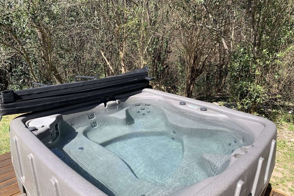 A hot tub with a wooden deck and a natural backdrop.
