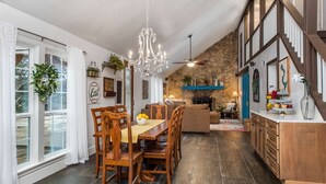 A spacious dining area with a wooden table and chairs, a chandelier, and a stone wall in the background.
