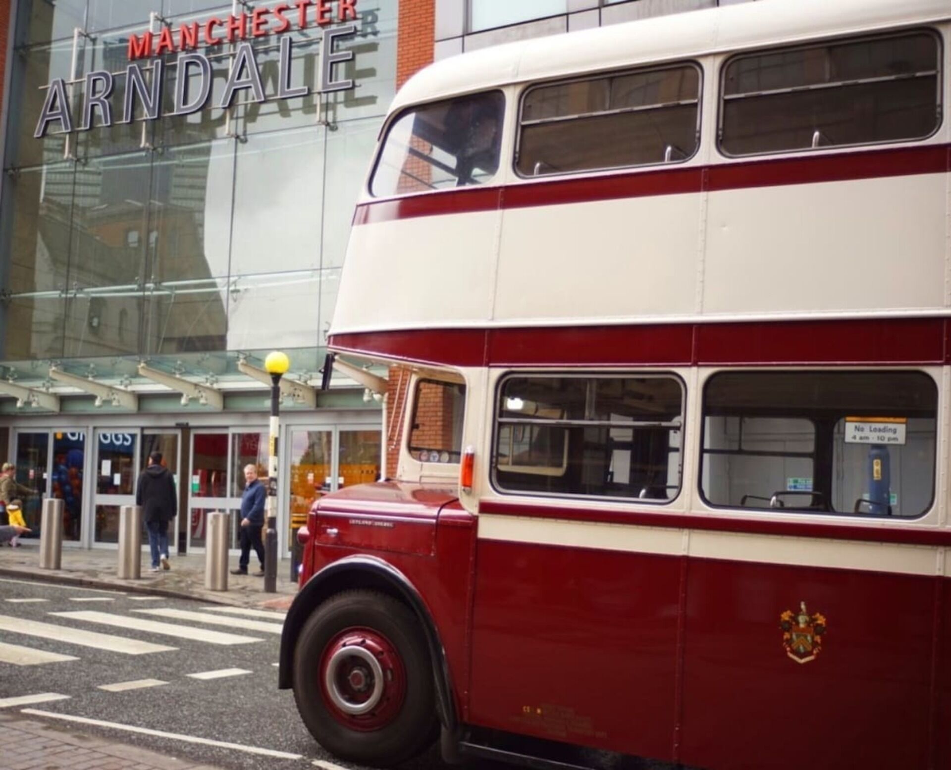 A red double-decker bus parked in front of a building with a sign that reads "Manchester Arndale".